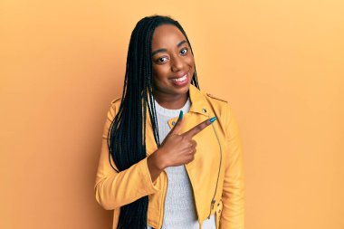 Yüzünde mutlu ve doğal bir ifade olan, elleri ve parmaklarıyla gülümseyen, rahat ceketli, Afro-Amerikalı genç bir kadın. 