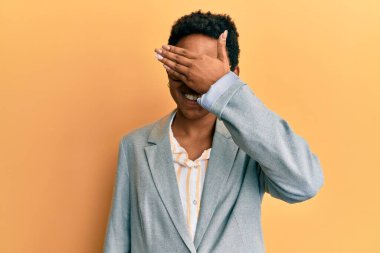 İş ceketi giyen, gözlüklü, gülümseyen ve gülen genç Afro-Amerikan kızı şaşırtmak için gözlerini kapatıyor. kör kavram. 