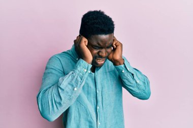 Gürültülü müzik sesi için günlük kıyafetler giyen yakışıklı siyahi adam kulaklarını parmaklarıyla kapatıyor. sağır kavramı. 