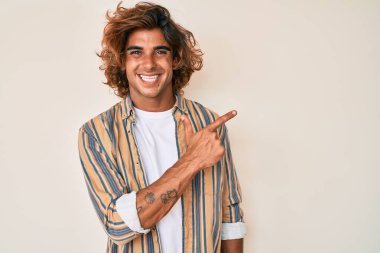 Gündelik giysiler giyen genç İspanyol adam gülümseyen, eli ve parmağı yana doğru gösteren. 