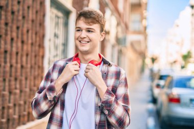 Genç beyaz adam şehirde kulaklık takarak mutlu bir şekilde gülümsüyor..