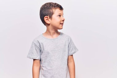 Yüzünde gülümseme ve doğal bir ifadeyle sıradan kıyafetler giyen sevimli sarışın çocuk. Kendinden emin gülen. 