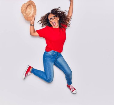 Orta yaşlı, güzel İspanyol bir kadın günlük kıyafetler giyiyor ve mutlu gülümsüyor. Yüzünde tebessümle beyaz arka planda şapkayla zıplıyor