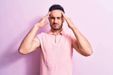 Genç, sakallı, sıradan polo giyen, pembe arka planda duran, eli başının üstünde duran yakışıklı bir adam. Stres yüzünden başı ağrıyor. Migren ağrısı..