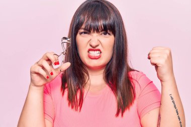 Kirpik bigudisi tutan genç ve cüsseli kadın öfkeyle bağırıyor, öfkeyle bağırıyor ve el kaldırıyor. 