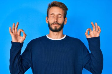 Sakallı, sıradan süveter giyen, gözleri kapalı gülümseyen ve parmaklarıyla meditasyon yapan yakışıklı beyaz adam. yoga konsepti. 