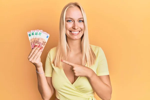 Ung Blond Flicka Håller Eurosedlar Ler Glad Pekar Med Hand — Stockfoto