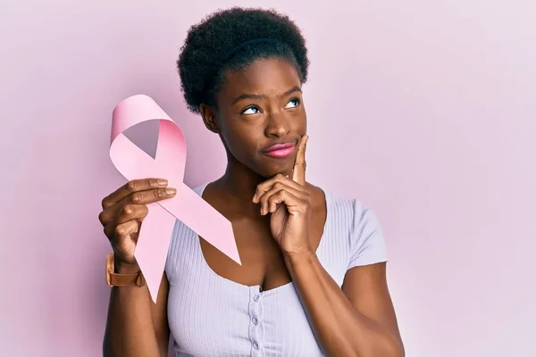 Młoda Afroamerykanka Trzymająca Różową Wstążkę Raka Poważna Twarz Myśląca Pytaniu — Zdjęcie stockowe