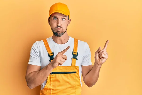 Jonge Knappe Man Draagt Klusjesman Uniform Wijzend Naar Zijkant Puffende — Stockfoto