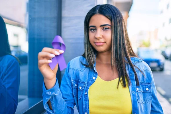 Young latin woman smiling happy holding purple ribbon at city.