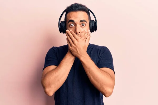 Young Hispanic Man Listening Music Using Headphones Shocked Covering Mouth — Stock Photo, Image