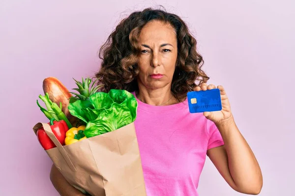 Mujer Hispana Mediana Edad Sosteniendo Comestibles Tarjetas Crédito Escéptico Nervioso —  Fotos de Stock