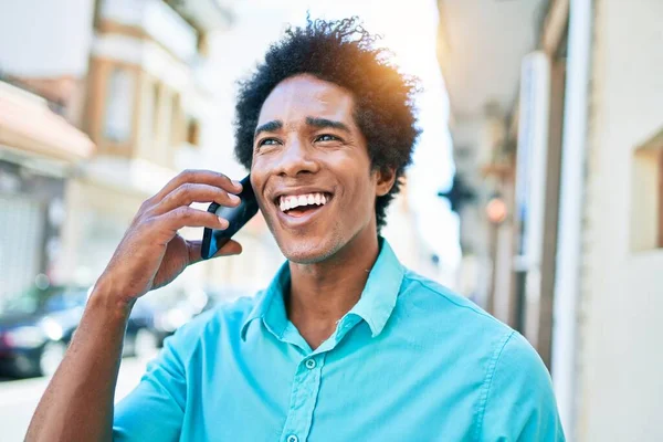 Genç, yakışıklı, Afro-Amerikan bir adam günlük giysiler giyip mutlu gülümsüyor. Yüzünde tebessümle dikilip şehrin caddesinde akıllı telefondan konuşuyor..
