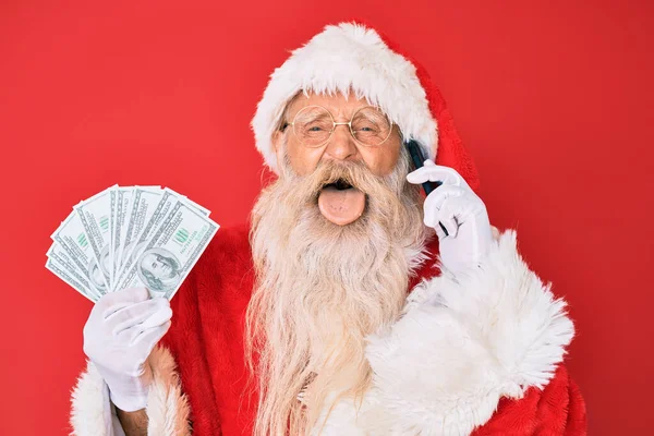 Staruszek Kostiumie Świętego Mikołaja Trzymający Dolary Smartfona Wystający Język Szczęśliwy — Zdjęcie stockowe