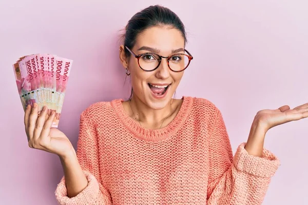 Young Caucasian Woman Holding 100000 Indonesian Rupiah Celebrating Achievement Happy — Stock Photo, Image