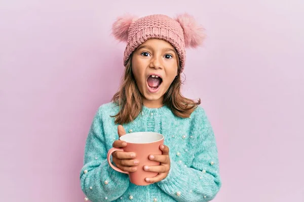 可愛いです女の子保持ピンクマグカップ身に着けていますかわいいウールの帽子祝うクレイジーと驚きのために成功とともにオープン目叫んで興奮 — ストック写真