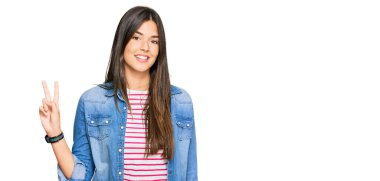 Genç esmer kadın, günlük kıyafetler giyip gülümsüyor ve parmaklarını zafer işareti yaparken kameraya bakıyor. İki numara.. 