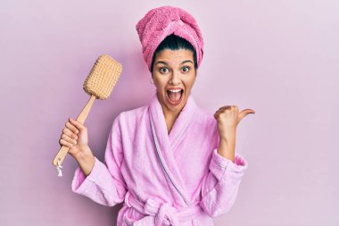 Duşta bornoz giyen genç İspanyol kadın elinde süngerle baş parmağını kaldırıp gülümseyerek ağzı açık gülümsüyor. 