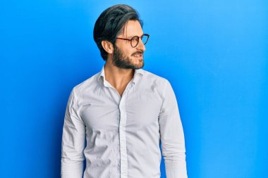 Gündelik kıyafetler ve gözlük takan genç İspanyol adam yan yan yan bakıyor, rahat poz veriyor ve kendine güvenen bir gülümseme takınıyor.. 