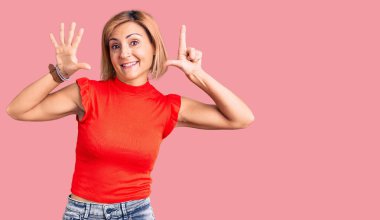 Genç sarışın kadın gündelik kıyafetler giyer ve yedinci parmaklarını göstererek gülümserken kendinden emin ve mutluydu.. 