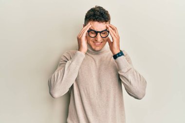 Balıkçı yaka kazak giyen İspanyol genç bir adam. Elleri kafasında, stresten baş ağrısı çekiyor. migren ağrısı. 