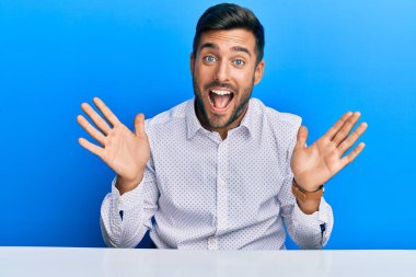 İş kıyafetleri giymiş yakışıklı İspanyol adam çılgın kutlamalar yapıyor ve kollarını kaldırıp heyecanla haykırarak başarıyı kutluyor. Kazanan konsept 