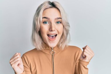 Gündelik giysiler giyen genç sarışın kız şaşkınlık ve şaşkınlık içinde kollarını kaldırarak ve gözlerini açarak başarıyı kutluyor. Kazanan konsept. 