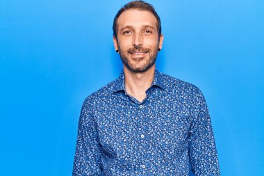 Gündelik kıyafetler giyen yakışıklı genç adam pozitif ve mutlu görünüyor. Duruyor ve gülümsüyor. Kendine güvenen bir gülümsemeyle dişlerini gösteriyor. 