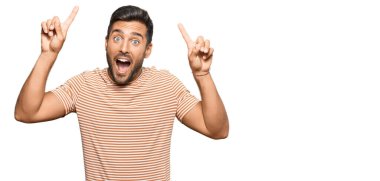 Yakışıklı, sıradan kıyafetler giyen, şaşkın şaşkın gülümseyen, parmaklarıyla işaret eden ve kollarını kaldıran bir İspanyol.. 