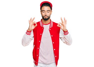 Sakallı genç adam beyzbol üniforması giyiyor rahatla ve gözleri kapalı gülümse parmaklarıyla meditasyon hareketi yapıyor. yoga konsepti. 