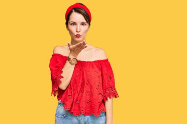 Kısa saçlı, kısa saçlı, günlük yaz kıyafetleri giyen ve kameraya bakan genç, esmer bir kadın. Havada el ele öpüşmek çok güzel ve seksi. aşk ifadesi. 