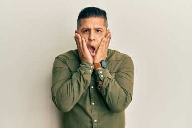 Gündelik kıyafetler giyen genç Latin adam korkmuş ve şok olmuş, şaşırmış ve şaşırmış bir yüz ifadesi var. 