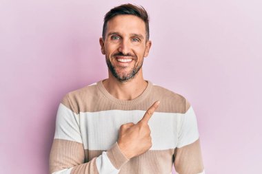 Sakallı, sıradan giyinmiş, neşeli gülümseyen, eli ve parmağı yanda olan yakışıklı bir adam. 