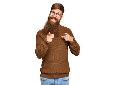 Genç İrlandalı kızıl elbiseli ve gözlüklü adam mutlu ve komik yüzlü parmaklarını kameraya doğrultuyor. iyi enerji ve titreşimler. 