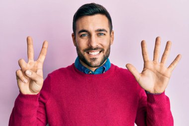 Gündelik kıyafetler giyen genç İspanyol adam yedi numarayı gösterip işaret ederken kendinden emin ve mutlu bir şekilde gülümsüyor.. 