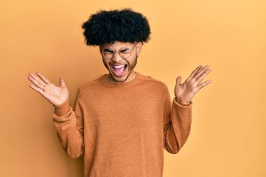 Afro saçlı genç Afrikalı bir adam sıradan bir kazak giyiyor ve başarı için deli ve çılgın bir kutlama yapıyor kolları havada ve gözleri kapalı heyecanla bağırıyor. Kazanan konsept 