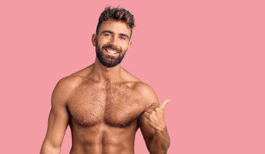 Mayo giyen, mutlu yüzüyle gülümseyen ve başparmağıyla yan tarafı gösteren İspanyol asıllı genç bir adam.. 