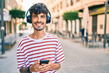 Şehrin caddesinde yürüyen, kulaklık ve akıllı telefon kullanan genç bir İspanyol..