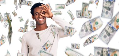 Kış süveteri giyen Afrikalı yakışıklı adam el hareketleriyle gülümsüyor ve mutlu yüzüyle parmaklarının arasından bakıyor..