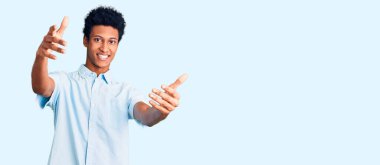 Gündelik giysiler giymiş genç Afro-Amerikan bir adam kameraya sarılıp gülümseyerek bakıyor. Mutluluğu kucaklayan neşeli bir ifade.. 