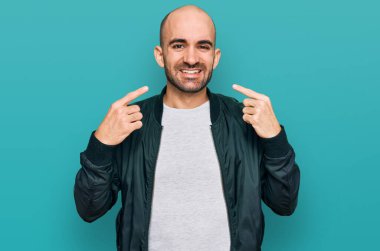 Günlük kıyafetler giyen, neşeli gülümseyen, parmaklarıyla ve ağzıyla işaret eden İspanyol genç bir adam. diş sağlığı kavramı. 