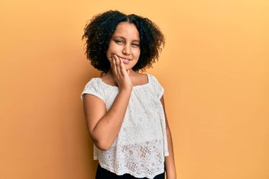 Afro saçlı, günlük kıyafetler giyen, diş ağrısı ya da diş hastalığından dolayı ağızlarına acı dolu bir ifadeyle dokunan küçük bir kız. dişçi 