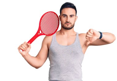 Kızgın yüzlü, tenis raketi tutan genç yakışıklı bir adam. Negatif işaret, baş parmakları aşağıda, reddedilme kavramı. 