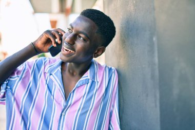 Genç Afrikalı Amerikalı gülümseyen adam şehrin caddesindeki akıllı telefonda mutlu bir şekilde konuşuyor..