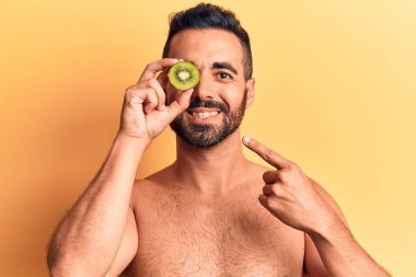 Genç İspanyol üstsüz bir adam elinde kivi tutarken mutlu bir şekilde elini ve parmağını gösterdi. 