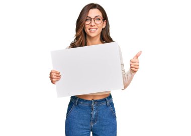 Genç esmer kadın boş afiş tutuyor mutlu ve olumlu gülümsüyor, başparmağıyla mükemmel ve onay işareti yapıyor. 