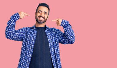 Günlük kıyafetler giyen, neşeli gülümseyen, parmaklarıyla ve ağzıyla işaret eden İspanyol genç bir adam. diş sağlığı kavramı. 