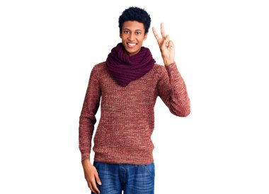 Genç Afro-Amerikan adam, günlük kışlık süveter ve atkı giymiş parmaklarını zafer işareti yaparken gösteren kameraya bakıp gülümsüyor. İki numara.. 