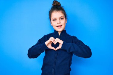 Sevimli İspanyol çocuk, gündelik giysiler içinde. Sevgiyle gülümsüyor. Kalp sembolü ve elleri ile şekil veriyor. romantik kavram. 