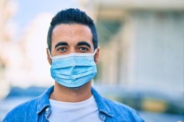 Tıbbi maske takan genç İspanyol adam şehirde dikiliyor..